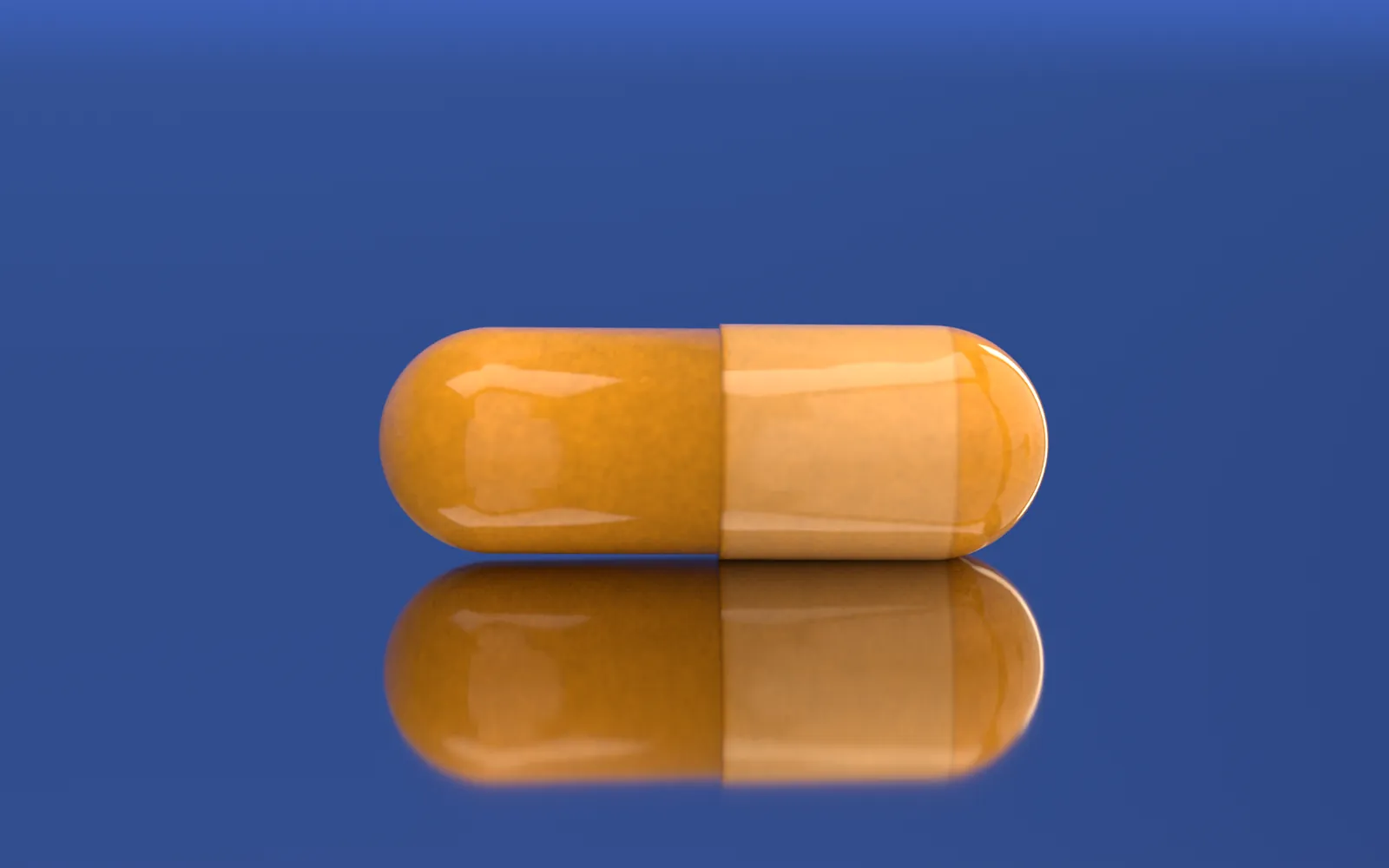 Macro: one closed turmeric capsule lying on polished steel over the cobalt paper, its mirror image below it.